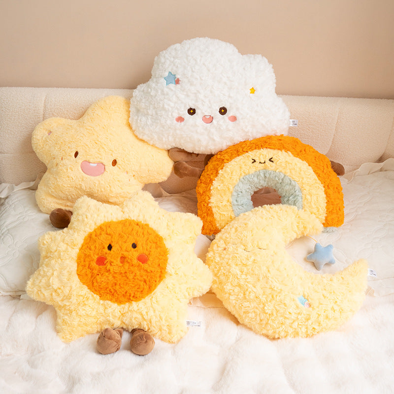 Collection of soft celestial-themed cushions featuring a smiling cloud, star, sun, rainbow, and crescent moon arranged on a bed.
